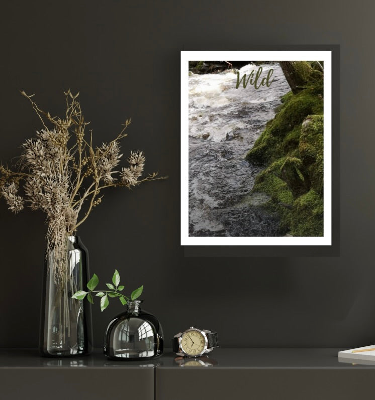 An A4 giclée print of a river and forest scene displayed on a shelf with decorative items, in a frame.