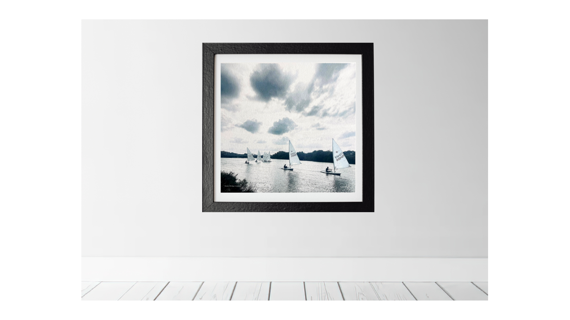 Framed photograph of the river Thames with sailboats on a white wall.