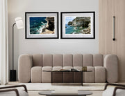 Two framed coastal landscapes above a beige sofa in a living room.
