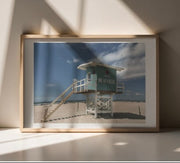 Framed photograph of a French beach scene with a lifeguard tower on a wall.