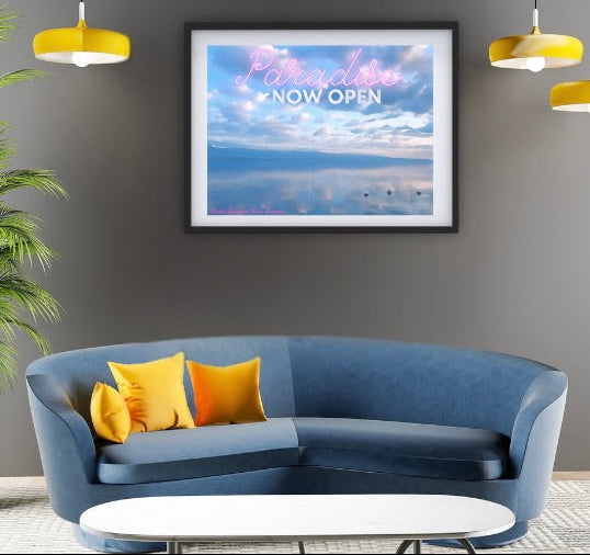 Modern living room with a blue sofa, yellow pillows, a plant, and framed blue Paradise now open artwork on a gray wall.