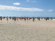 A wide sandy beach in Deauville, France with its signature colourful parasols arranged in rows under a blue sky with white clouds, with the ocean visible in the distance.