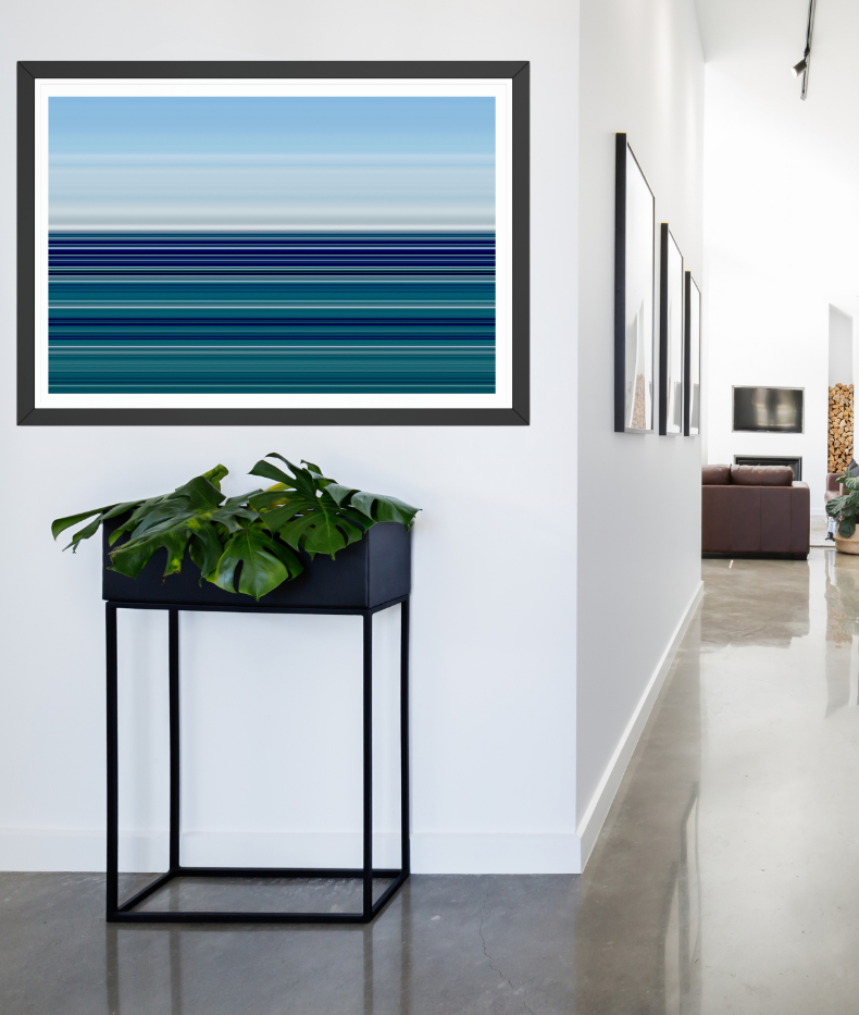 A framed horizontal art print featuring blue and teal stripes, displayed on a white wall in a modern hallway above a black metal stand with a green plant.
