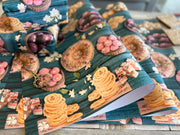 A vibrant wrapping paper featuring traditional Indian sweets like ladoos, barfi, and jalebis on a rich teal wooden background. Decorated with jasmine flowers and intricate details, this seamless pattern adds a festive, cultural touch, perfect for celebrations.