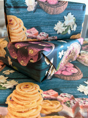 A vibrant wrapping paper featuring traditional Indian sweets like ladoos, barfi, and jalebis on a rich teal wooden background. Decorated with jasmine flowers and intricate details, this seamless pattern adds a festive, cultural touch, perfect for celebrations.