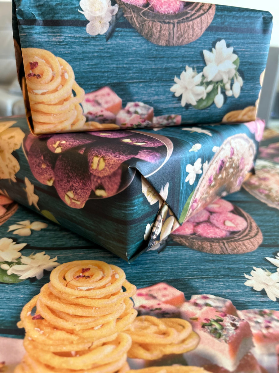 A vibrant wrapping paper featuring traditional Indian sweets like ladoos, barfi, and jalebis on a rich teal wooden background. Decorated with jasmine flowers and intricate details, this seamless pattern adds a festive, cultural touch, perfect for celebrations.
