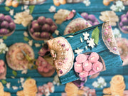 A vibrant wrapping paper featuring traditional Indian sweets like ladoos, barfi, and jalebis on a rich teal wooden background. Decorated with jasmine flowers and intricate details, this seamless pattern adds a festive, cultural touch, perfect for celebrations.