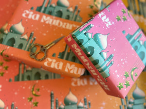 A festive Eid wrapping paper featuring a majestic mosque on a pink-to-orange graduated background. Adorned with twinkling stars, crescent moons, and elegant Eid Mubarak text, this design captures the joy and spirituality of Eid celebrations.