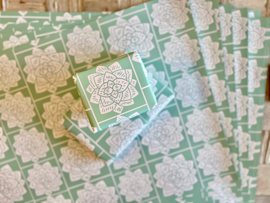 Wrapping paper inspired by Sindhi Ajrak block printing. Intricate white geometric & floral motifs on mint-green background. The repeating symmetrical pattern reflects traditional craftsmanship with a modern twist.