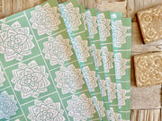 Wrapping paper inspired by Sindhi Ajrak block printing. Intricate white geometric & floral motifs on mint-green background. The repeating symmetrical pattern reflects traditional craftsmanship with a modern twist.