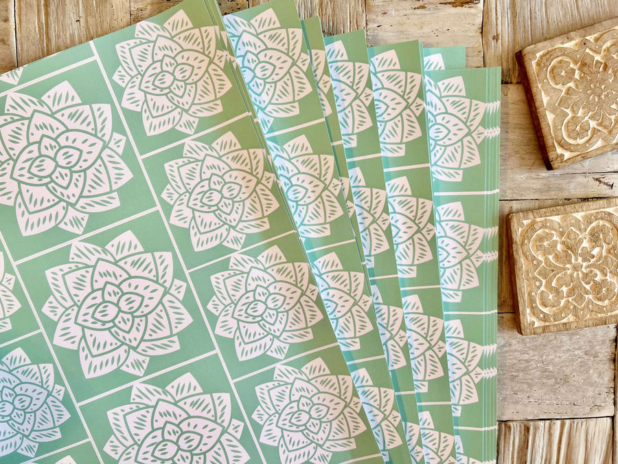 Wrapping paper inspired by Sindhi Ajrak block printing. Intricate white geometric & floral motifs on mint-green background. The repeating symmetrical pattern reflects traditional craftsmanship with a modern twist.