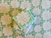 Wrapping paper inspired by Sindhi Ajrak block printing. Intricate white geometric & floral motifs on mint-green background. The repeating symmetrical pattern reflects traditional craftsmanship with a modern twist.
