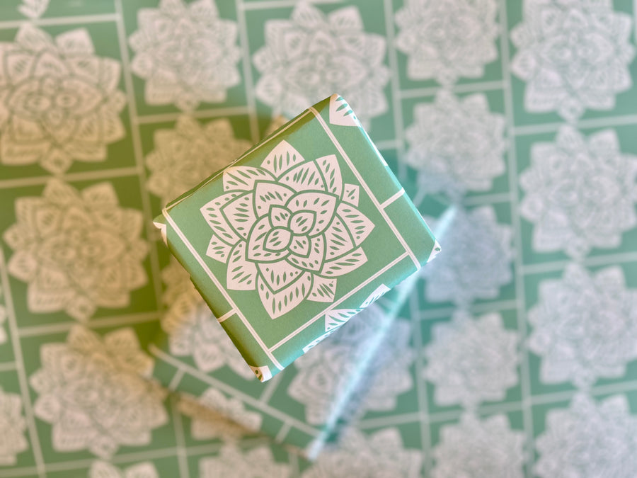 Wrapping paper inspired by Sindhi Ajrak block printing. Intricate white geometric & floral motifs on mint-green background. The repeating symmetrical pattern reflects traditional craftsmanship with a modern twist.