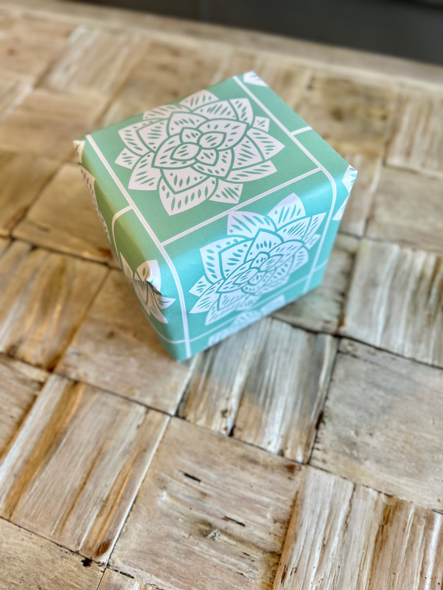 Wrapping paper inspired by Sindhi Ajrak block printing. Intricate white geometric & floral motifs on mint-green background. The repeating symmetrical pattern reflects traditional craftsmanship with a modern twist.