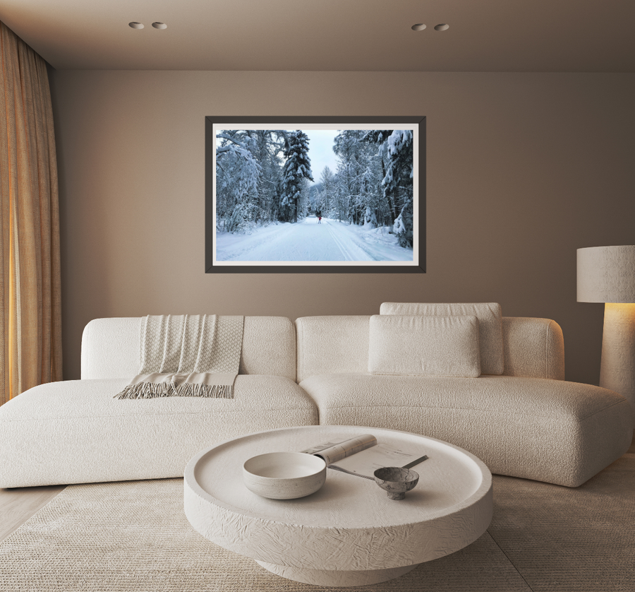 A framed landscape art print of a snowy forest path hangs on a beige wall above a modern white sectional sofa in a cozy living room setting.