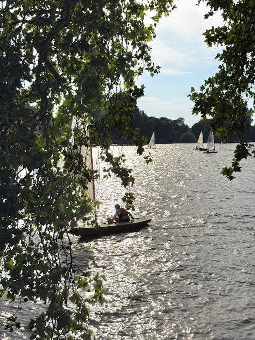 A small sailboat on a shimmering River Thames fine art photograph taken by Seafoam Atelier photographer, Samira Malik.  