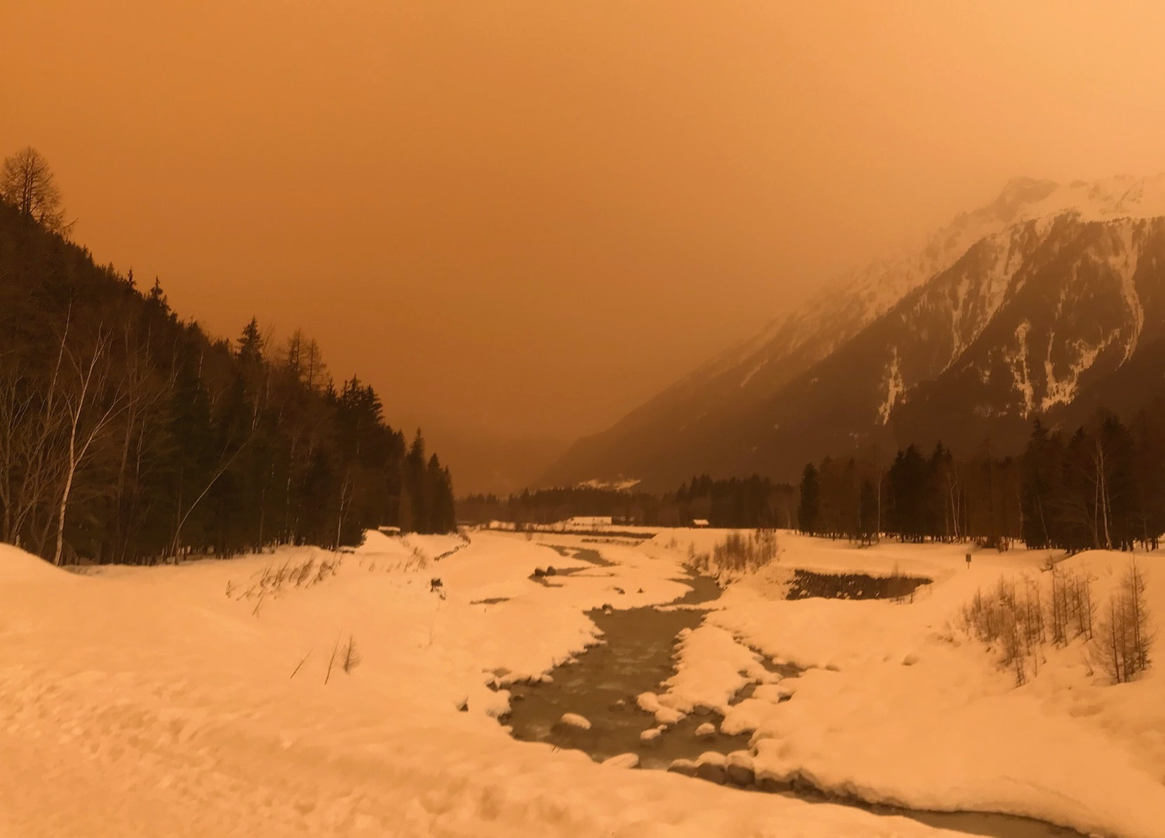 Chamonix snowy mountain valley under a hazy orange sky laden with sand travelled from the Sahara desert.